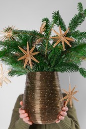 Photo of Woman holding beautiful Christmas composition of decorated fir tree branches on light background