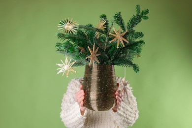 Photo of Woman holding beautiful Christmas composition of decorated fir tree branches on light green background