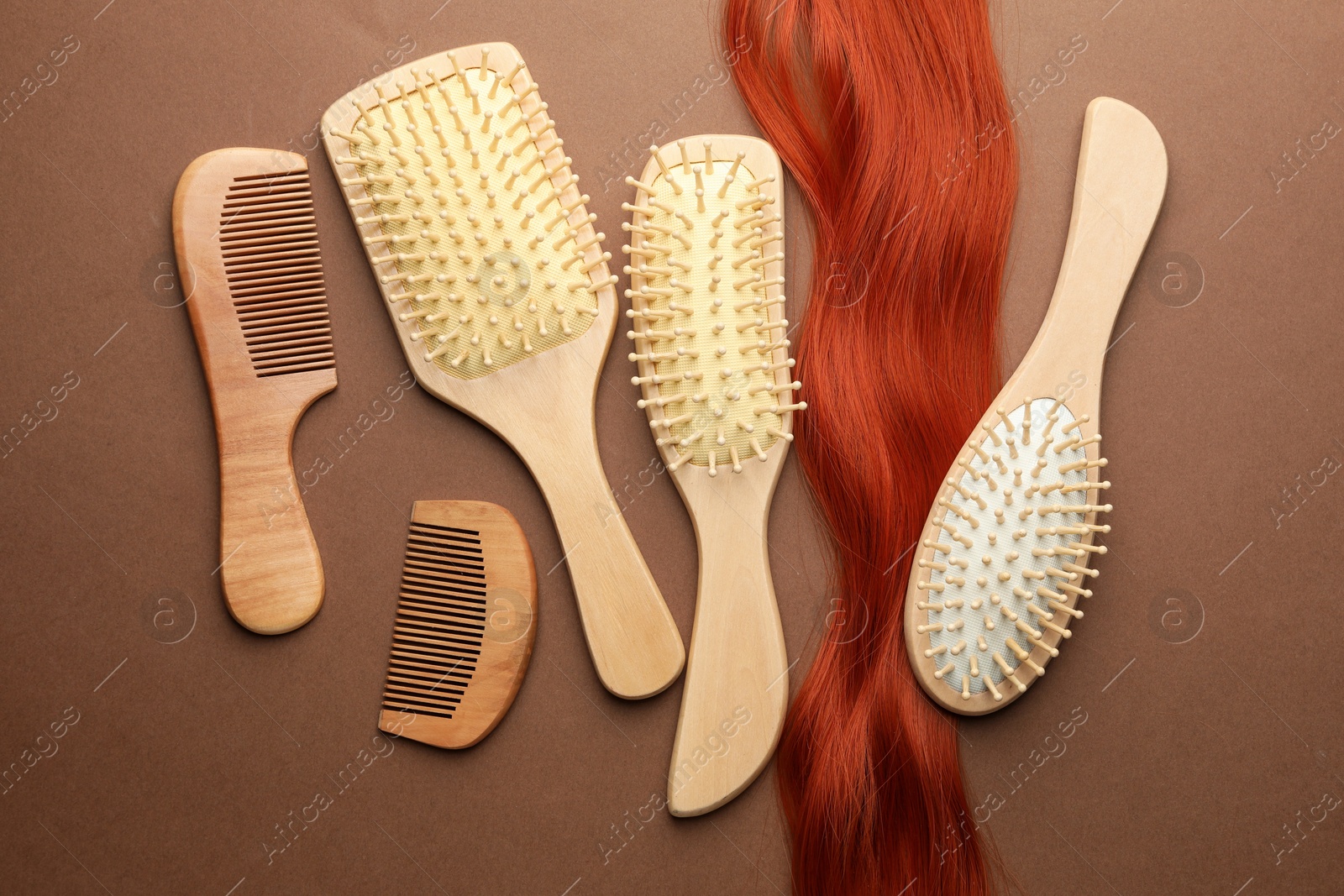 Photo of Set of different wooden brushes, combs and lock of hair on brown background, flat lay