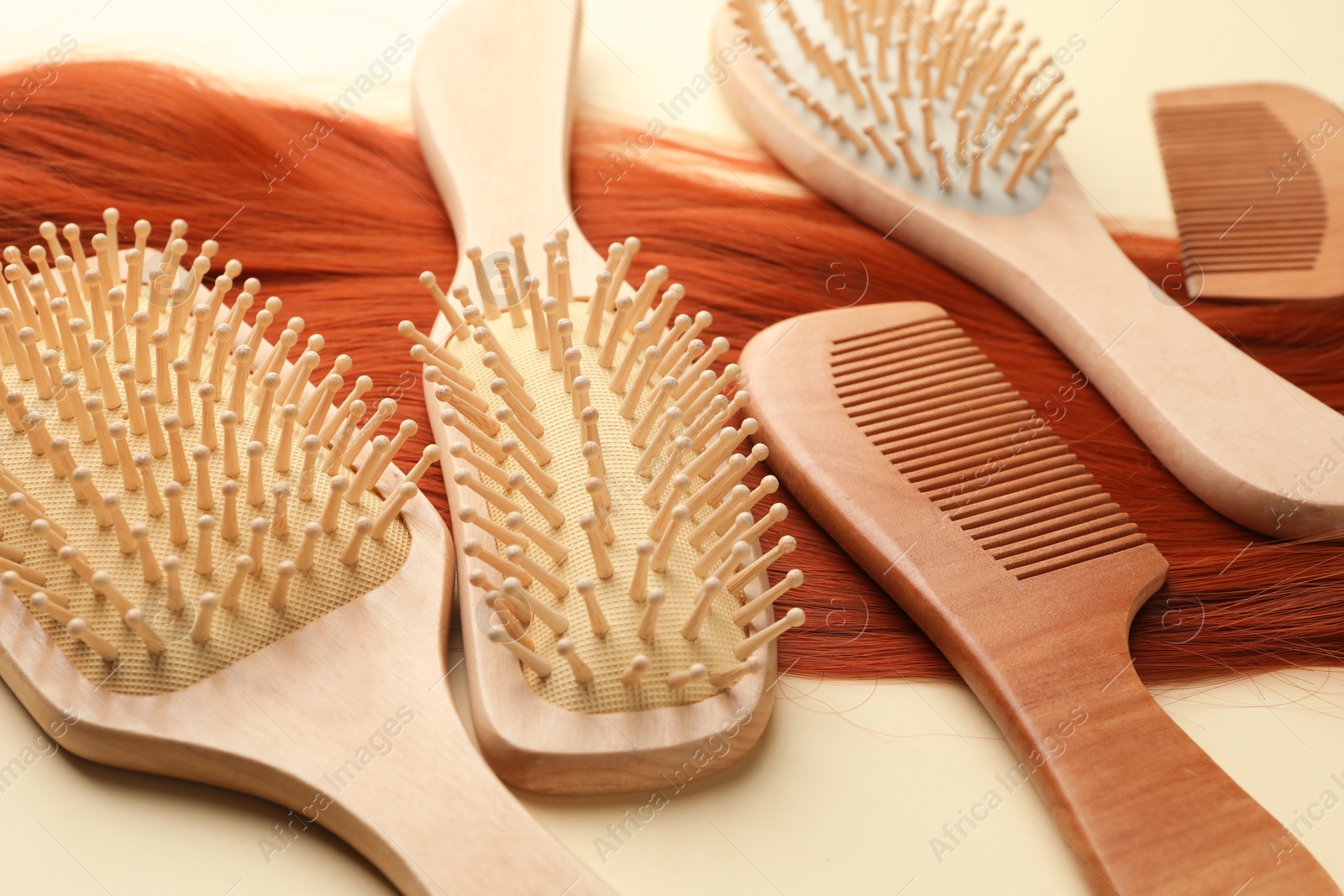 Photo of Set of different wooden brushes, combs and lock of hair on beige background, closeup