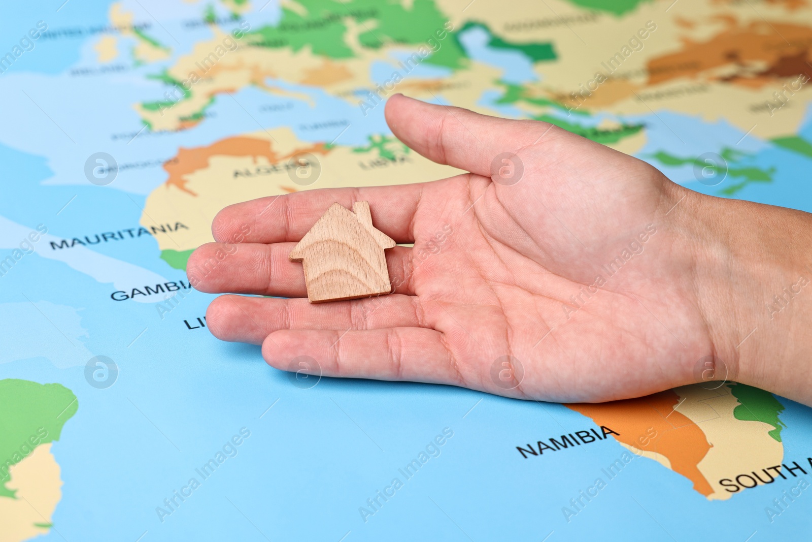 Photo of Woman holding wooden house model on world map, closeup. Accommodation search