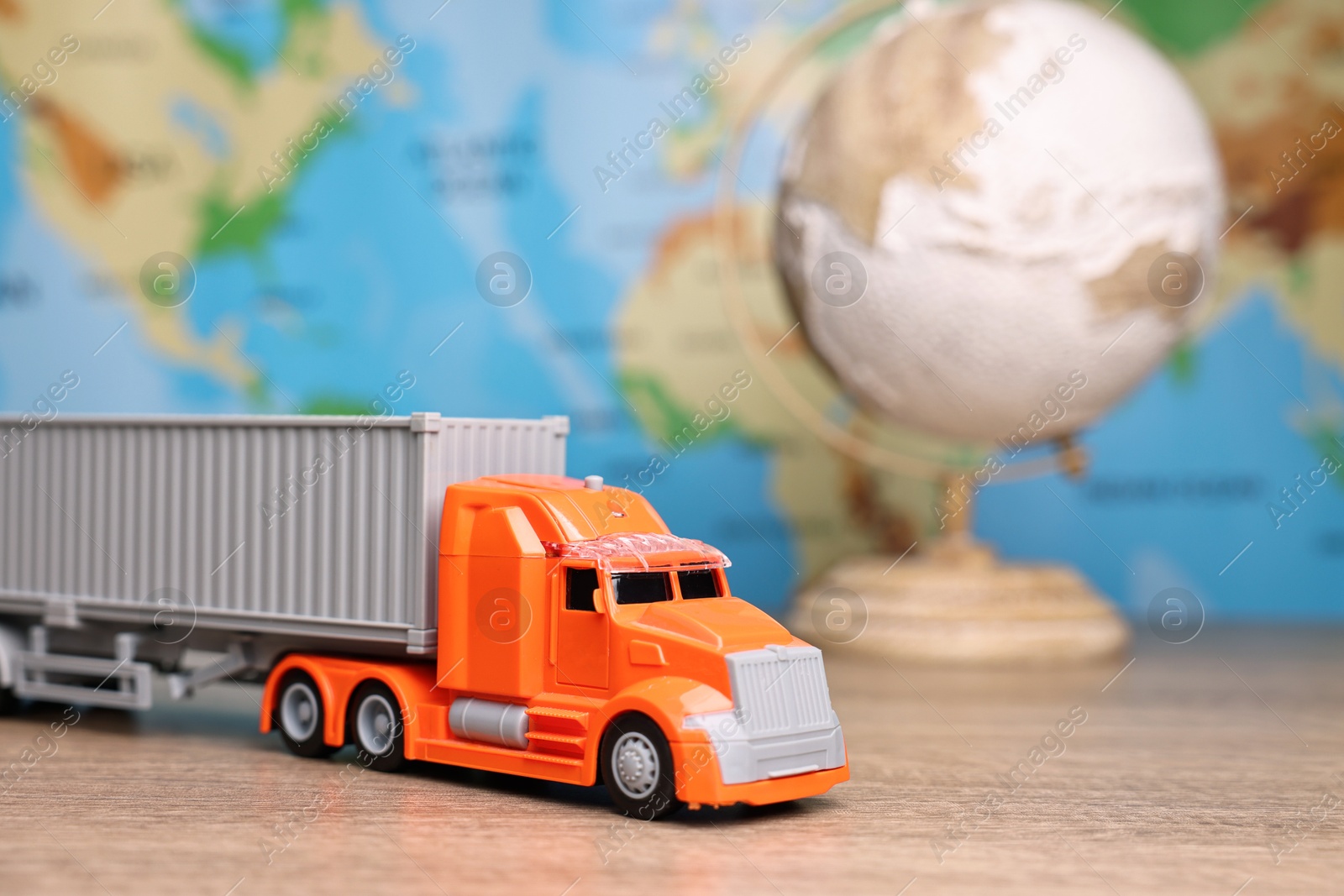 Photo of Toy truck and globe on wooden table against world map, closeup. Logistics concept