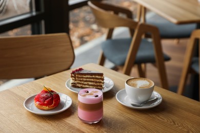 Photo of Aromatic coffee and delicious desserts served on wooden table in cafe