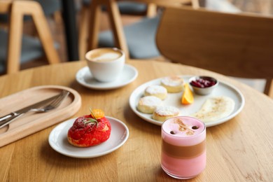 Photo of Delicious cottage cheese pancakes, dessert and coffee served on wooden table in cafe