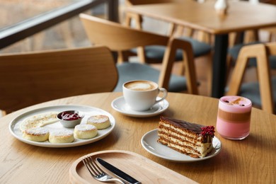 Photo of Delicious cottage cheese pancakes, cake and coffee served on wooden table in cafe