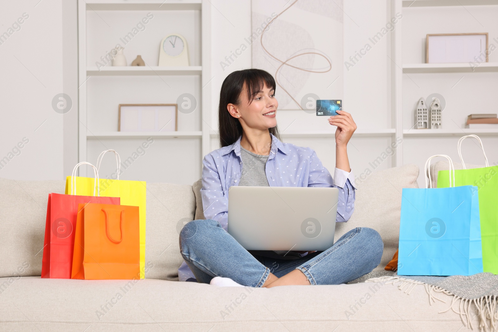 Photo of Internet shopping. Happy woman with credit card, laptop and colorful bags on sofa at home