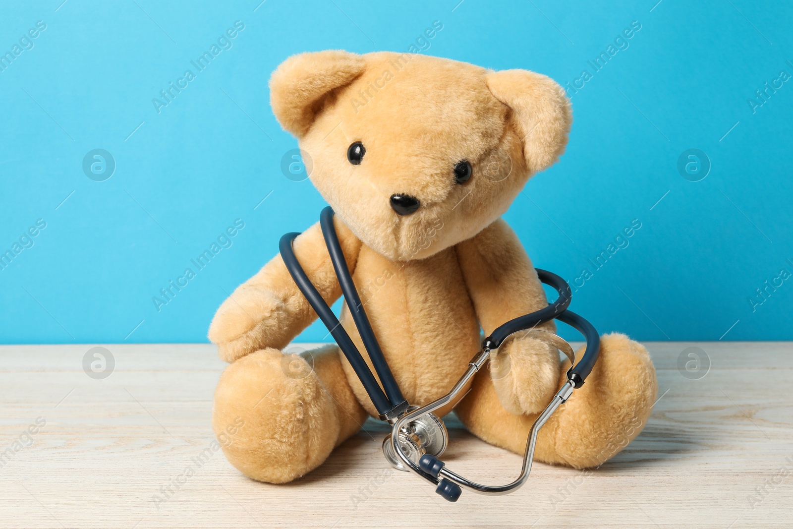 Photo of Pediatrics concept. Teddy bear with stethoscope on wooden table against light blue background