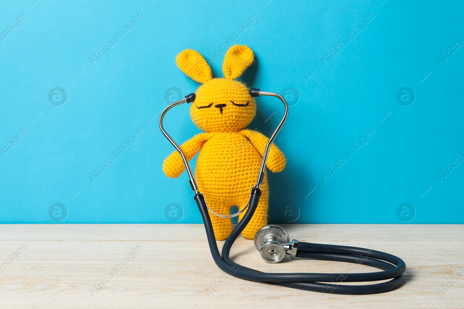 Photo of Pediatrics concept. Toy bunny with stethoscope on wooden table against light blue background