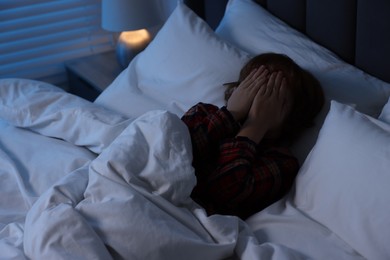 Photo of Scared boy covering face with hands in bed at night