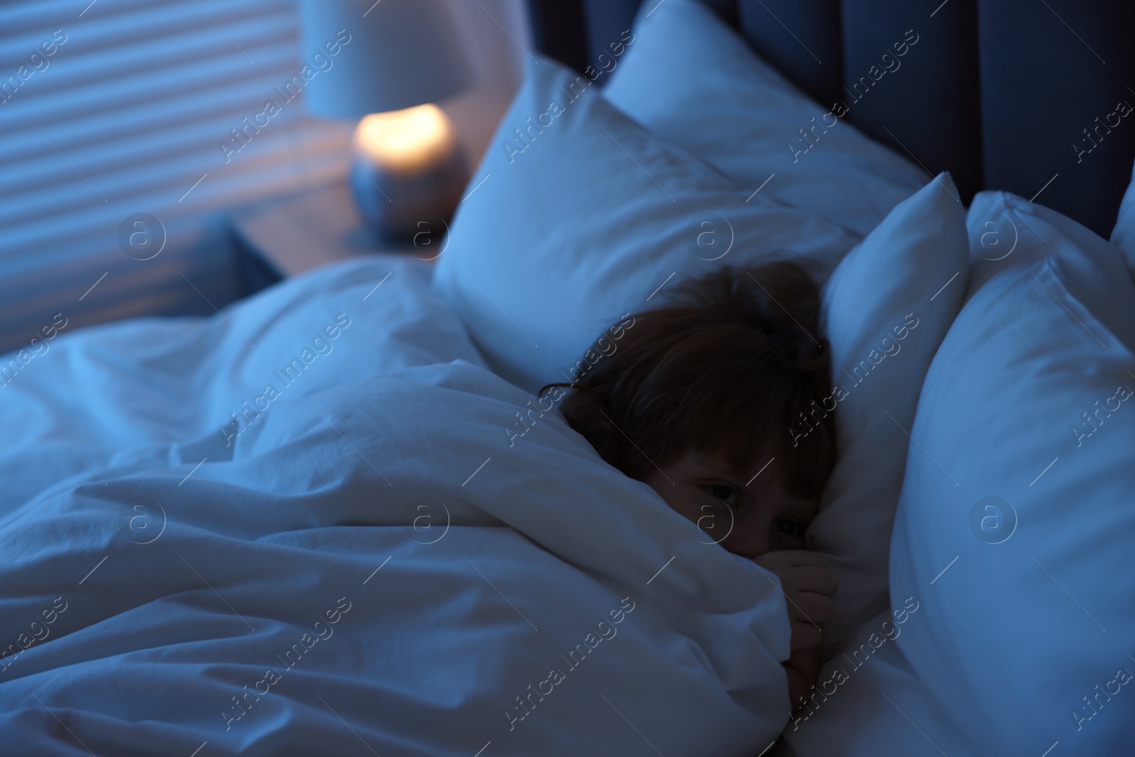 Photo of Scared boy hiding under duvet in bed at night