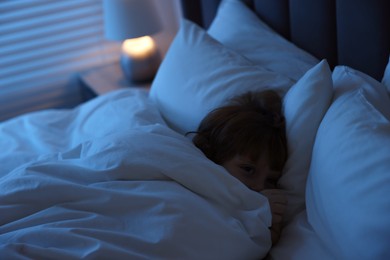 Scared boy hiding under duvet in bed at night