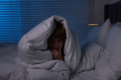 Scared boy hiding under duvet in bed at night