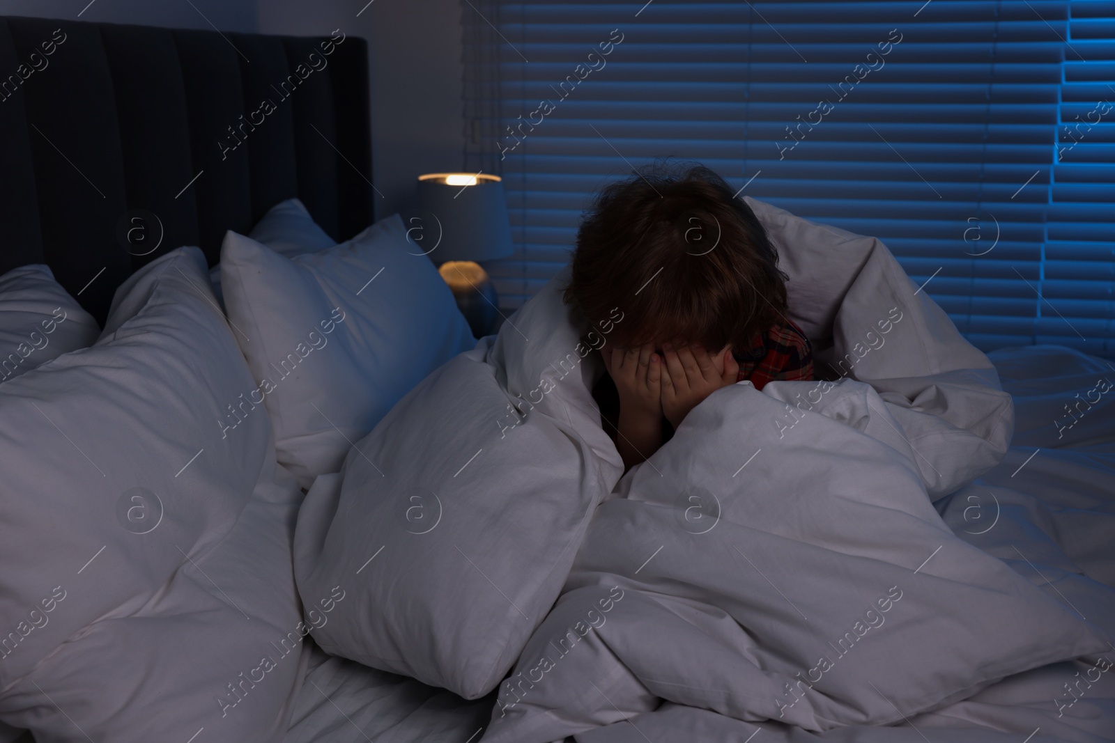 Photo of Scared boy wrapped in duvet on bed at night