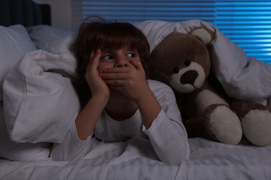 Photo of Scared boy with teddy bear in bed at night