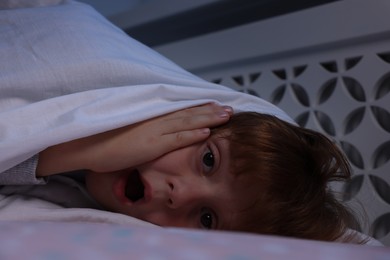 Photo of Afraid boy under blanket on bed at night