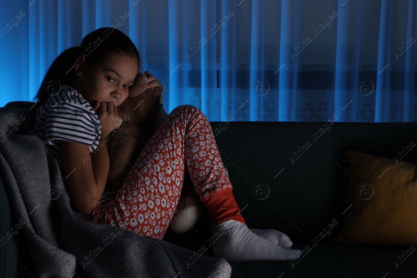 Photo of Afraid girl with teddy bear on sofa at home. Space for text