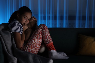 Photo of Afraid girl with teddy bear on sofa at home. Space for text