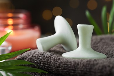 Photo of Spa stones, towel and green leaf against background with blurred lights, closeup