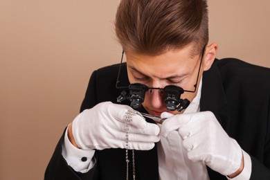 Photo of Appraiser with tweezers evaluating luxury necklace on beige background