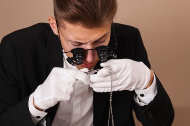 Photo of Appraiser with tweezers evaluating luxury necklace on beige background