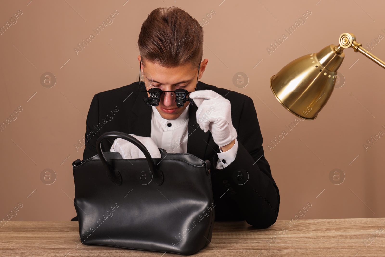 Photo of Appraiser evaluating leather bag at wooden table against beige background