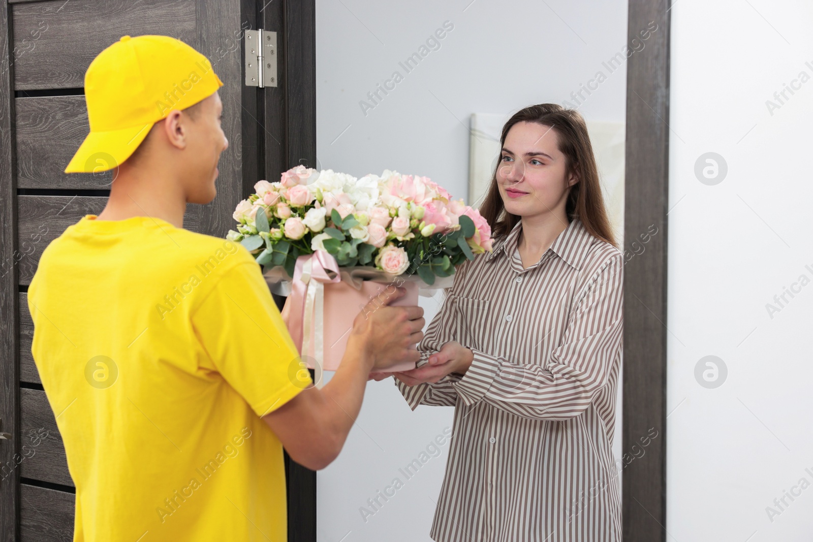 Photo of Delivery man giving gift box with beautiful floral composition to woman at door