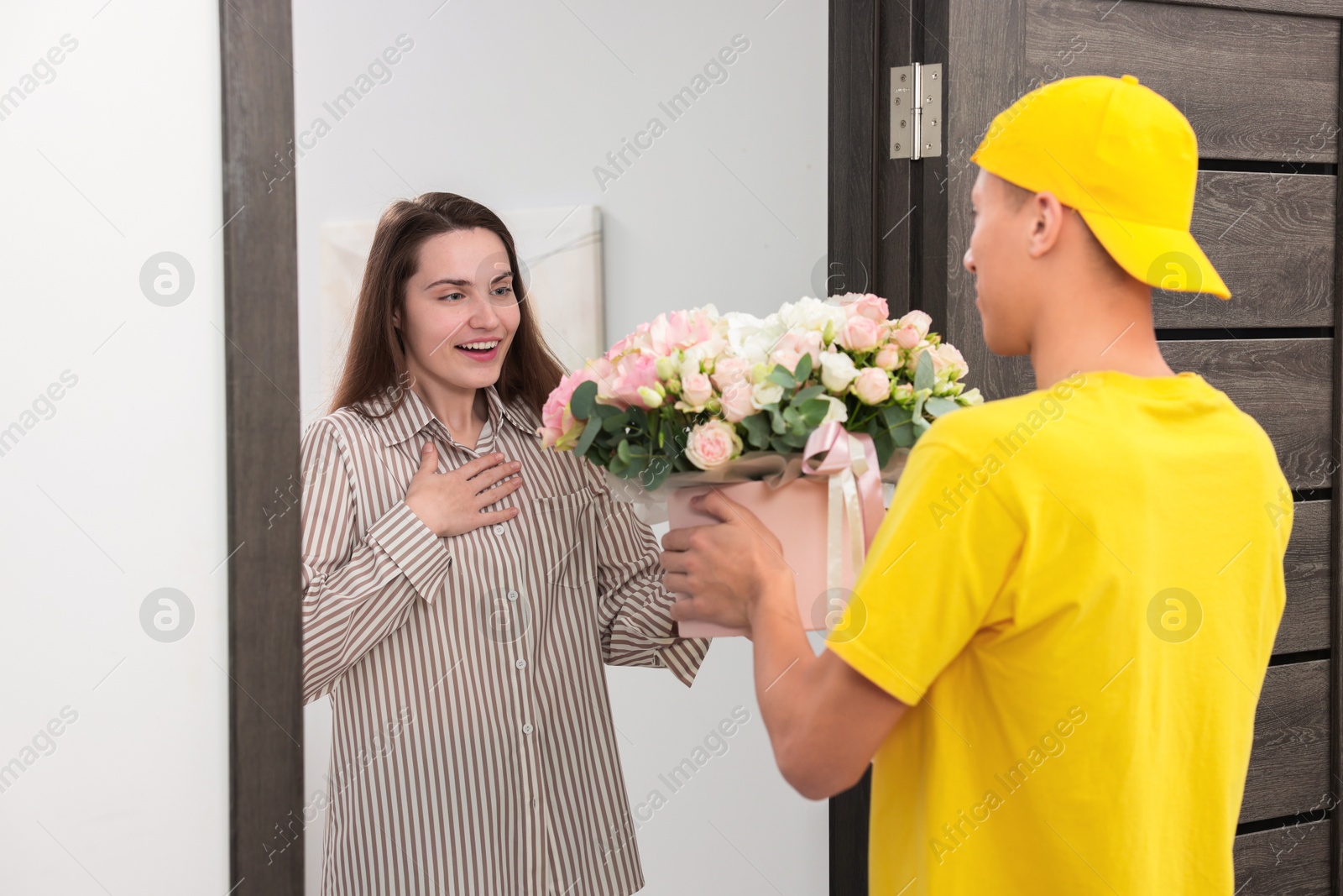 Photo of Delivery man giving gift box with beautiful floral composition to surprised woman at door