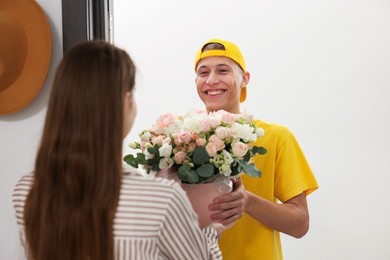 Photo of Happy delivery man giving gift box with beautiful floral composition to woman at door