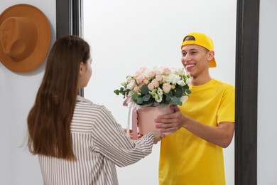 Photo of Happy delivery man giving gift box with beautiful floral composition to woman at door