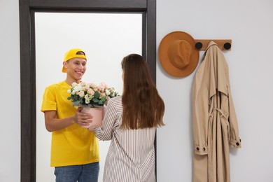 Photo of Happy delivery man giving gift box with beautiful floral composition to woman at door