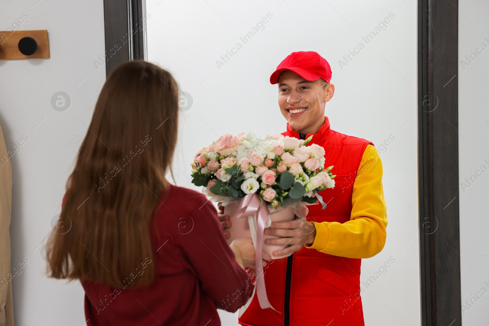 Photo of Happy delivery man giving gift box with beautiful floral composition to woman at door