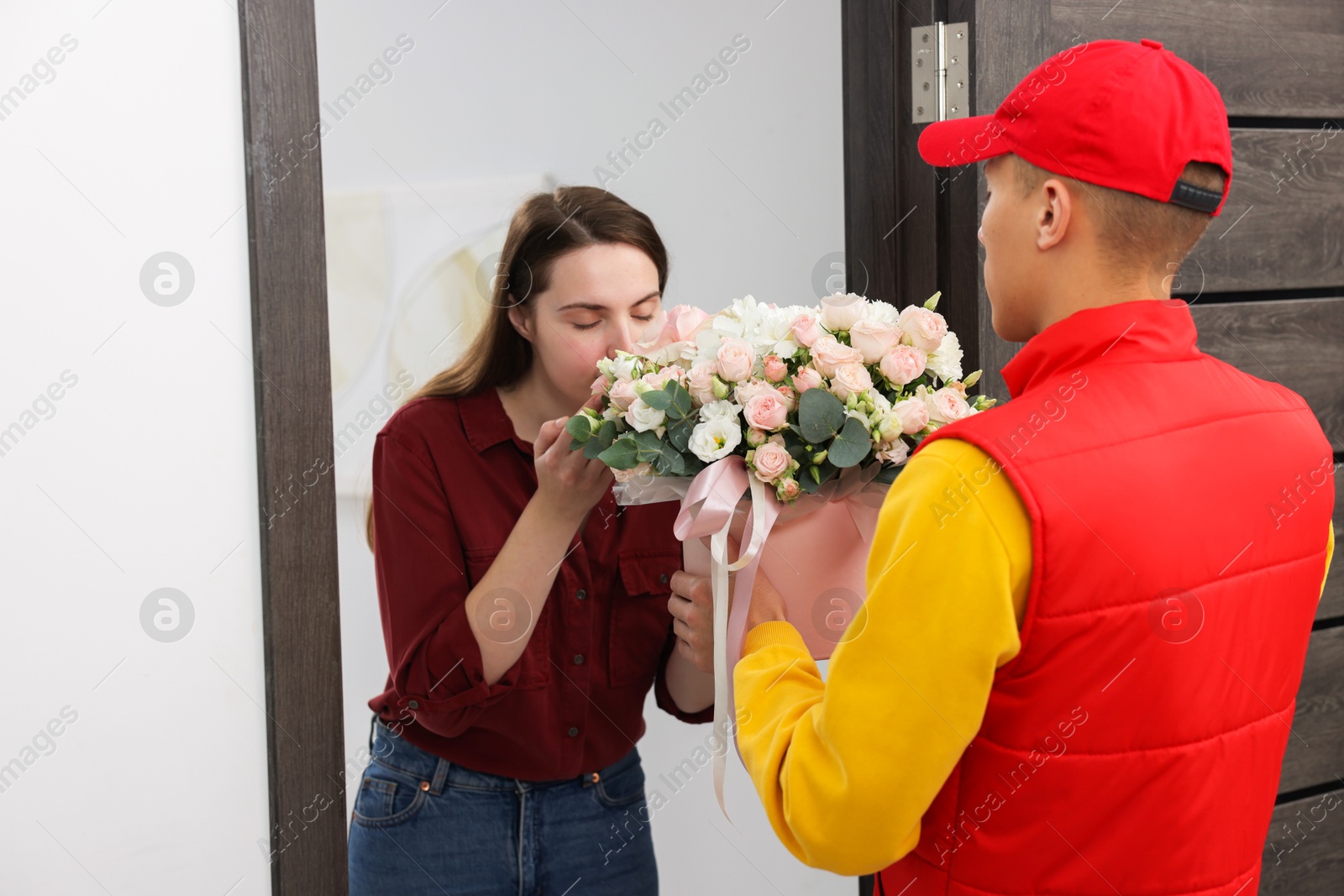 Photo of Woman smelling beautiful flowers from delivery man at door