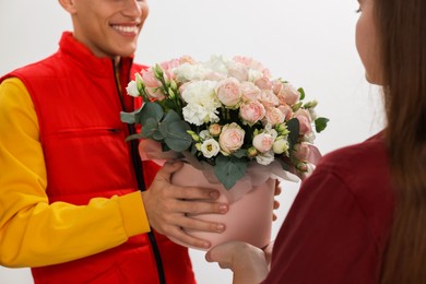 Photo of Smiling delivery man giving gift box with beautiful floral composition to woman, closeup