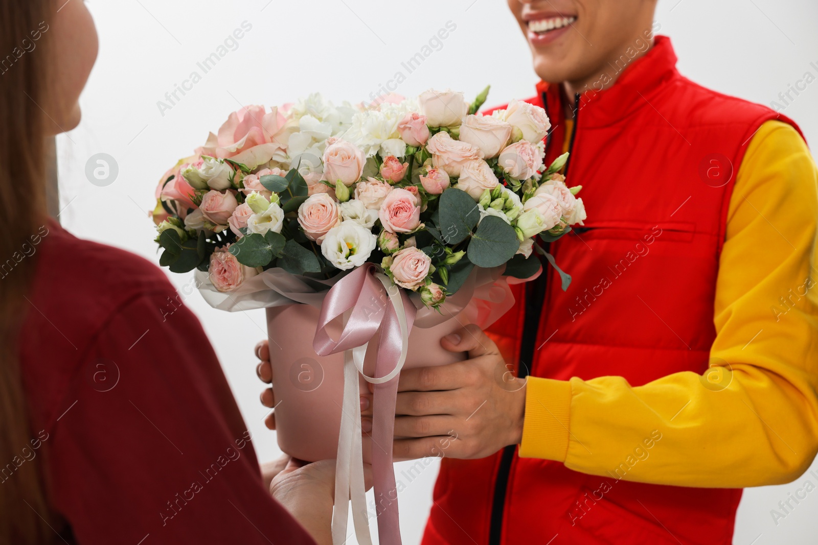 Photo of Smiling delivery man giving gift box with beautiful floral composition to woman, closeup