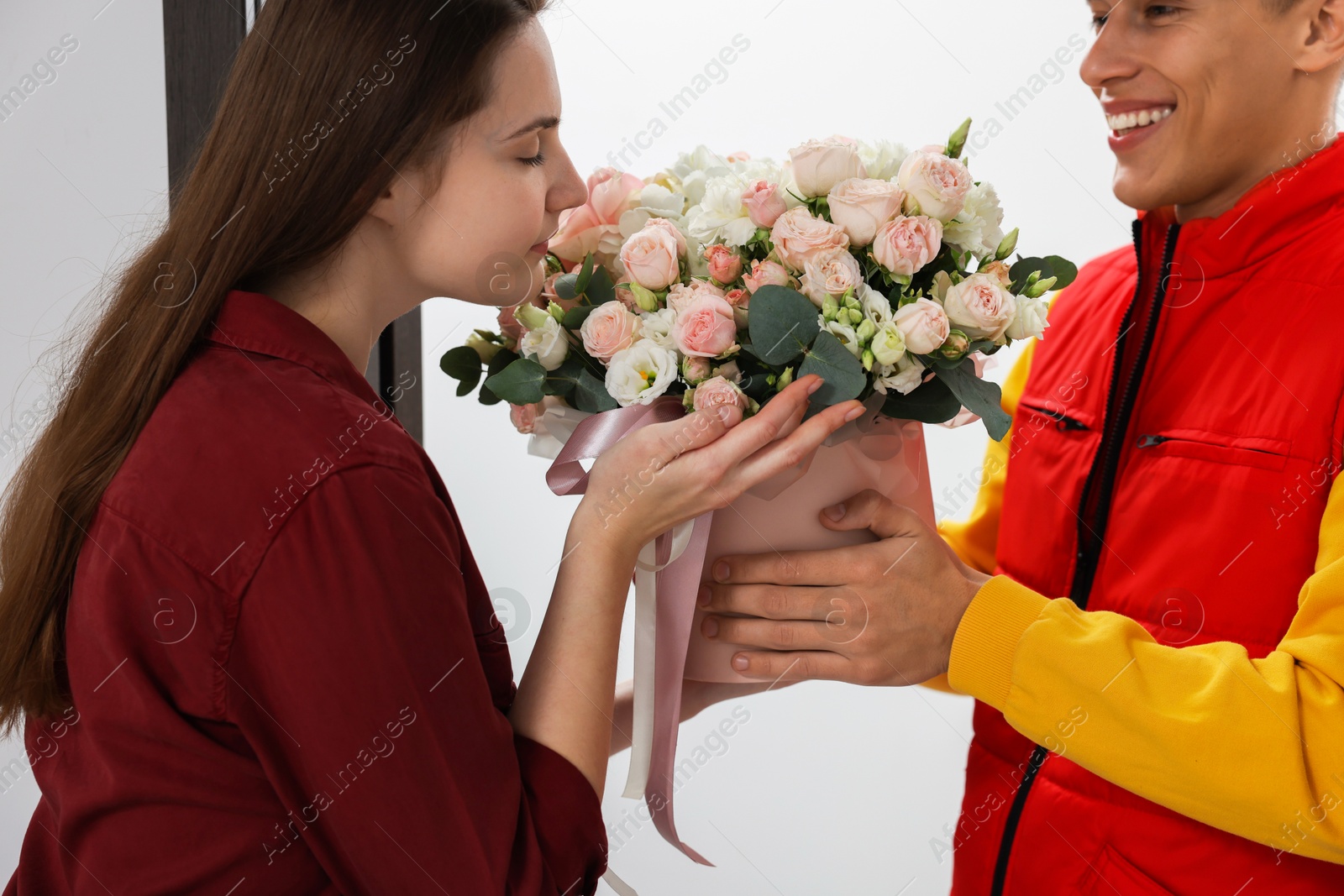 Photo of Smiling delivery man giving gift box with beautiful floral composition to woman, closeup