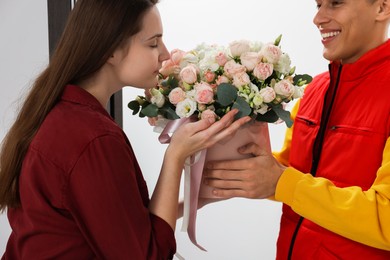 Photo of Smiling delivery man giving gift box with beautiful floral composition to woman, closeup