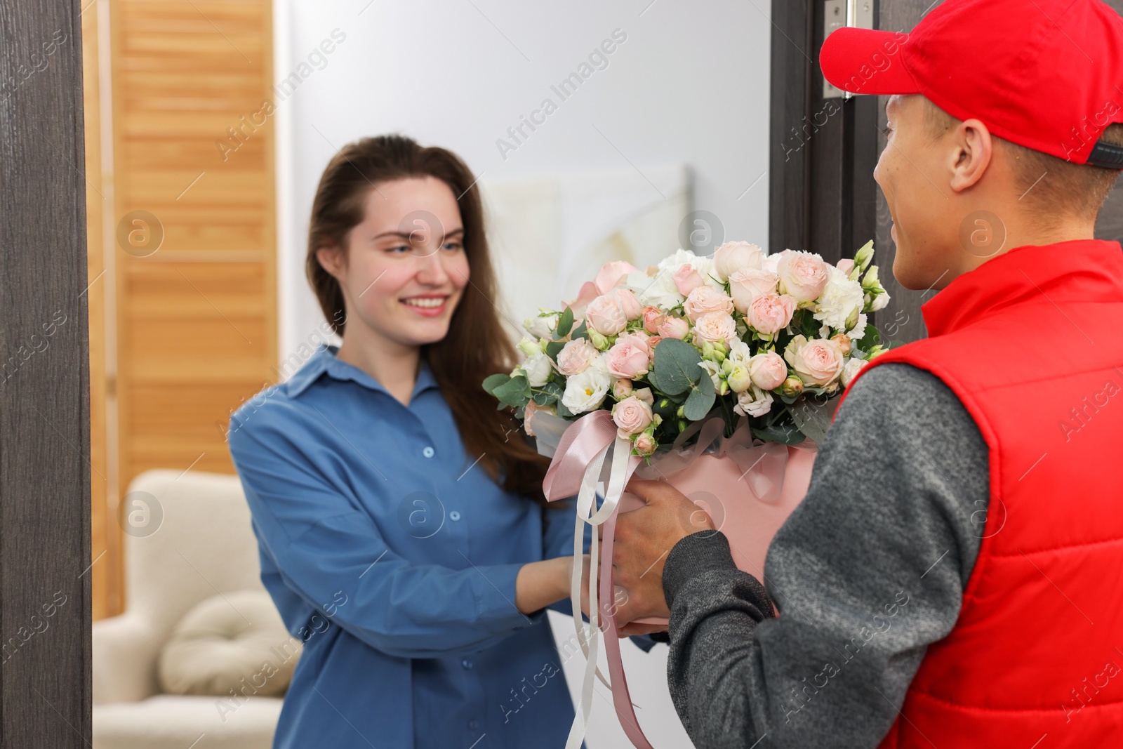 Photo of Happy woman receiving gift box with beautiful floral composition from delivery man at door