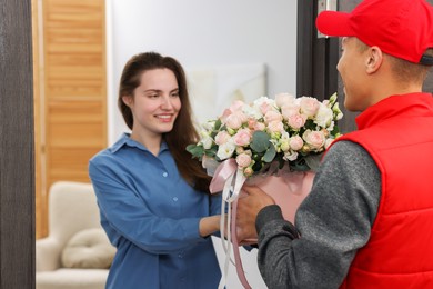 Happy woman receiving gift box with beautiful floral composition from delivery man at door