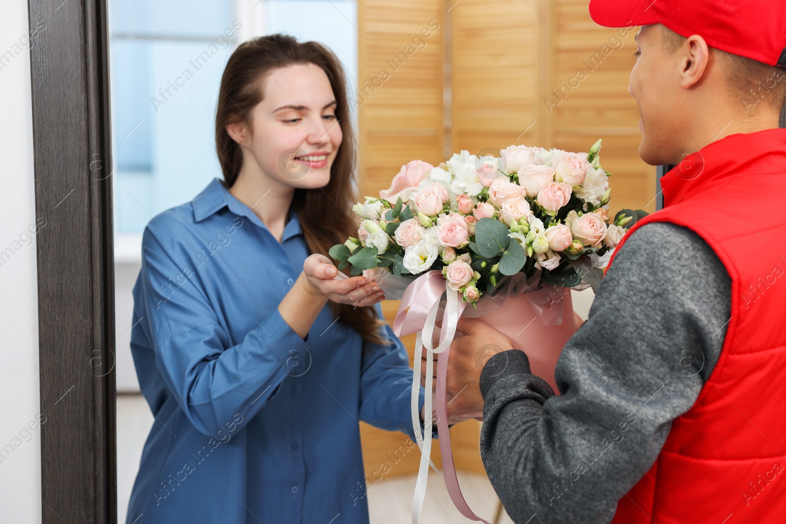 Photo of Happy woman receiving gift box with beautiful floral composition from delivery man at door