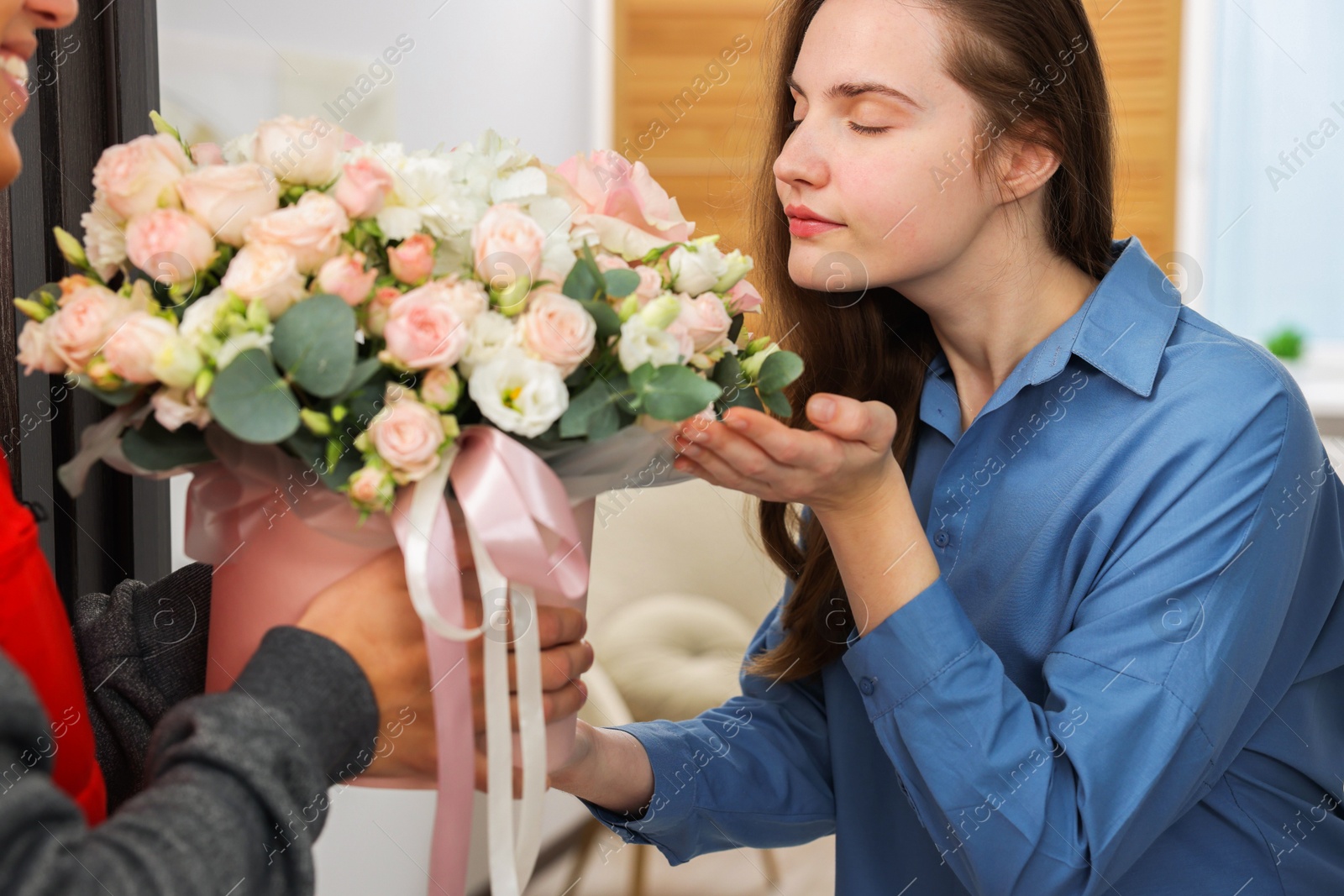 Photo of Woman smelling beautiful flowers from delivery man at door