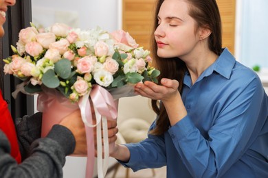 Photo of Woman smelling beautiful flowers from delivery man at door