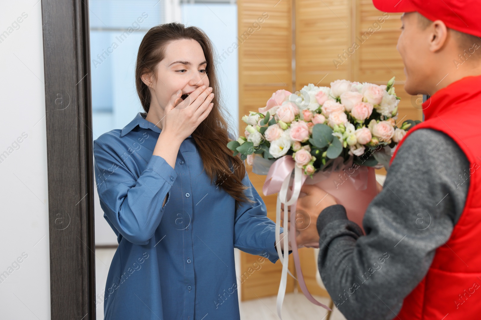 Photo of Surprised woman receiving gift box with beautiful floral composition from delivery man at door