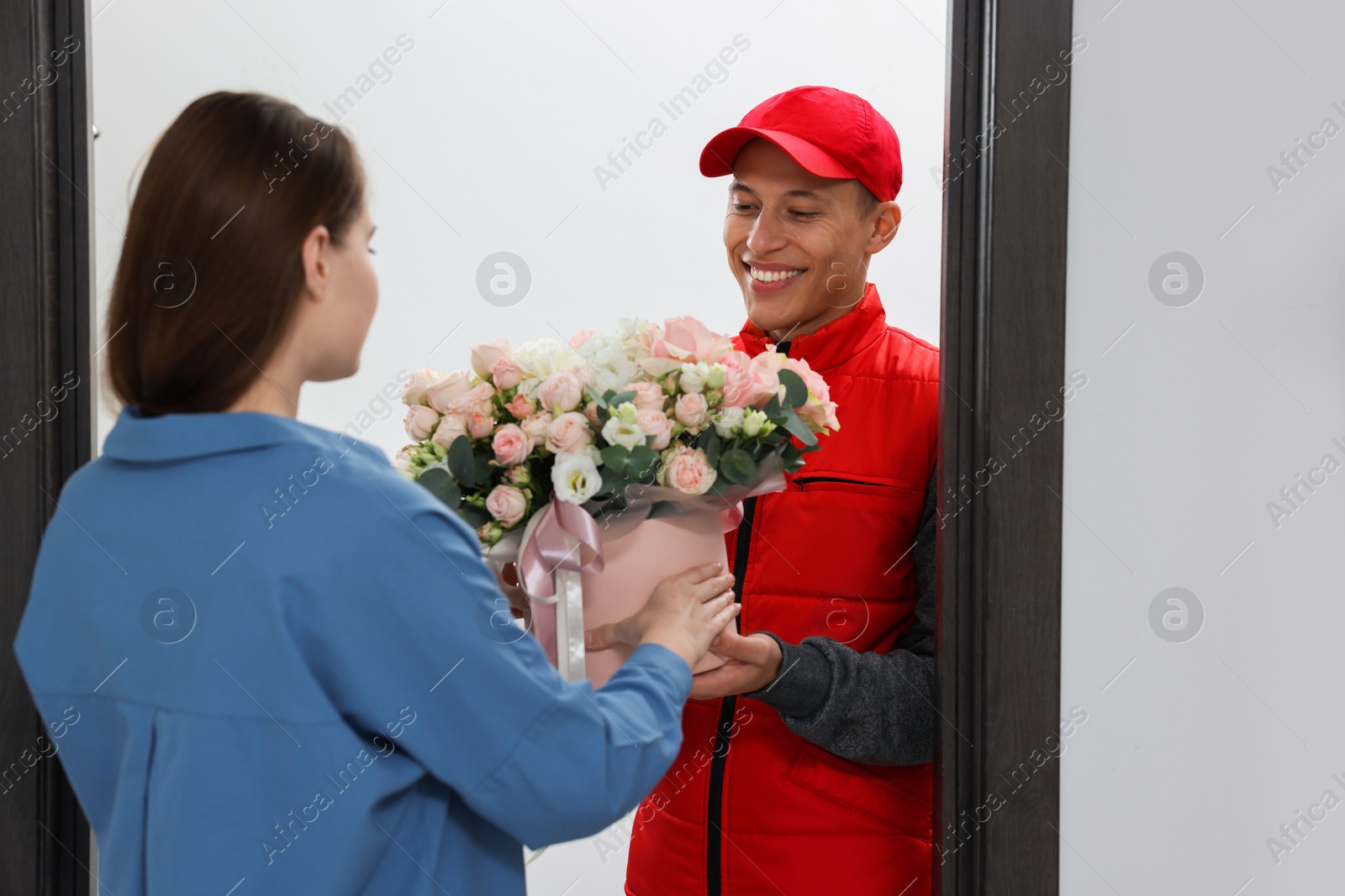 Photo of Smiling delivery man giving gift box with beautiful floral composition to woman at door