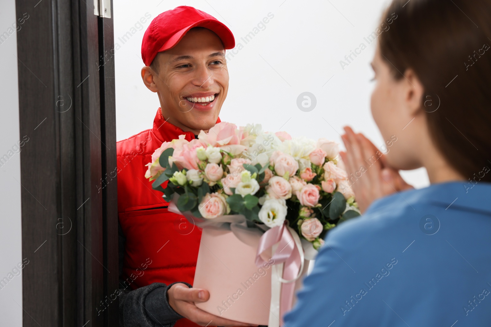 Photo of Smiling delivery man giving gift box with beautiful floral composition to woman at door