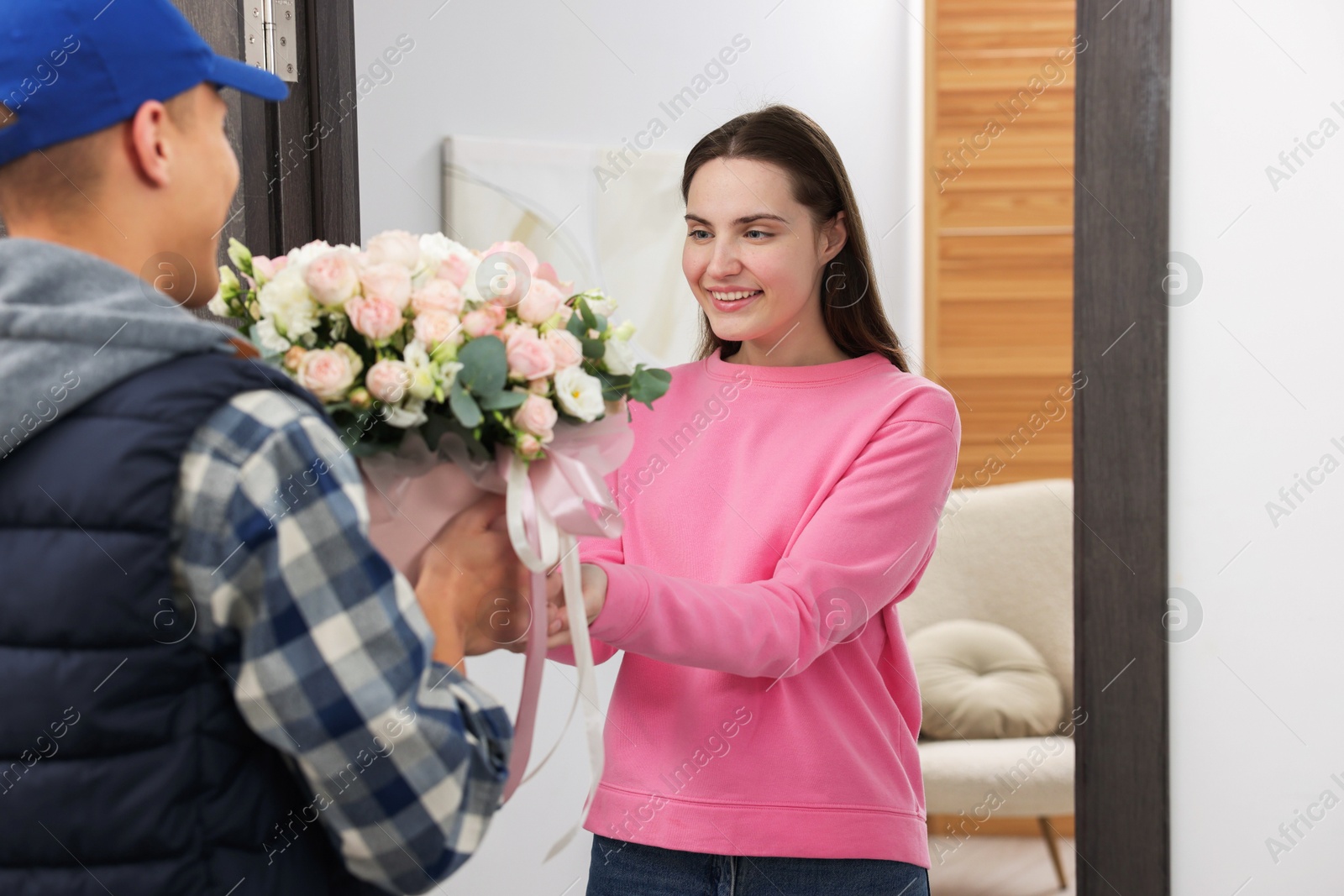 Photo of Happy woman receiving gift box with beautiful floral composition from delivery man at door