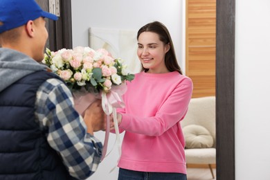 Photo of Happy woman receiving gift box with beautiful floral composition from delivery man at door