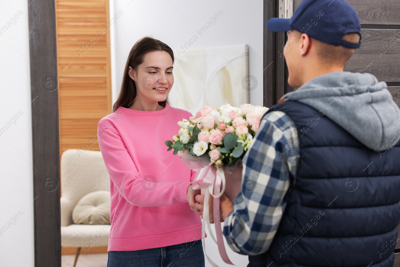 Photo of Happy woman receiving gift box with beautiful floral composition from delivery man at door