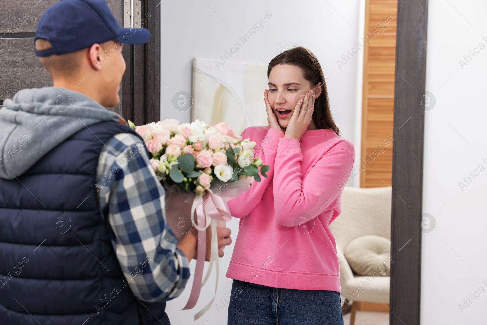 Photo of Surprised woman receiving gift box with beautiful floral composition from delivery man at door