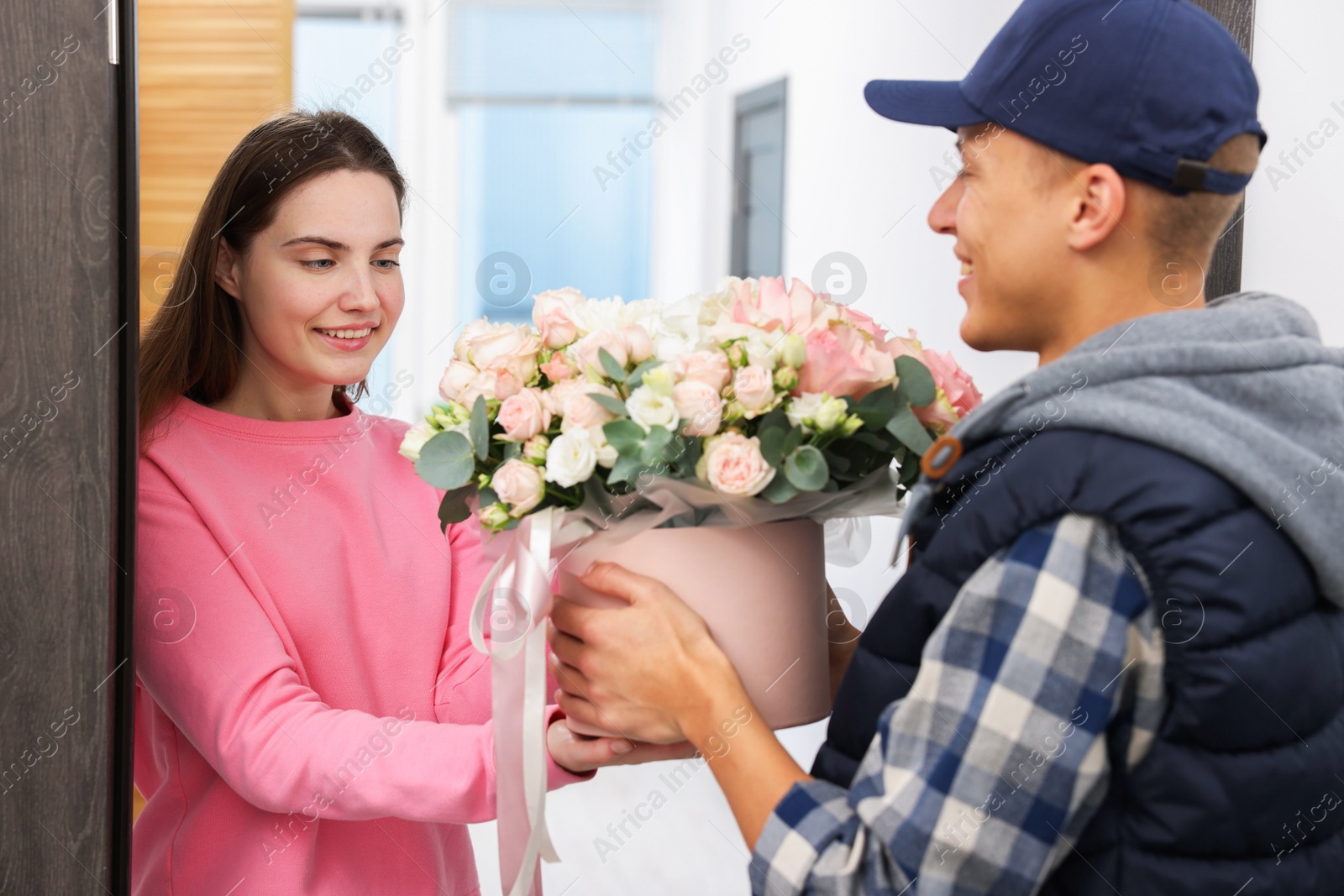 Photo of Happy woman receiving gift box with beautiful floral composition from delivery man at door