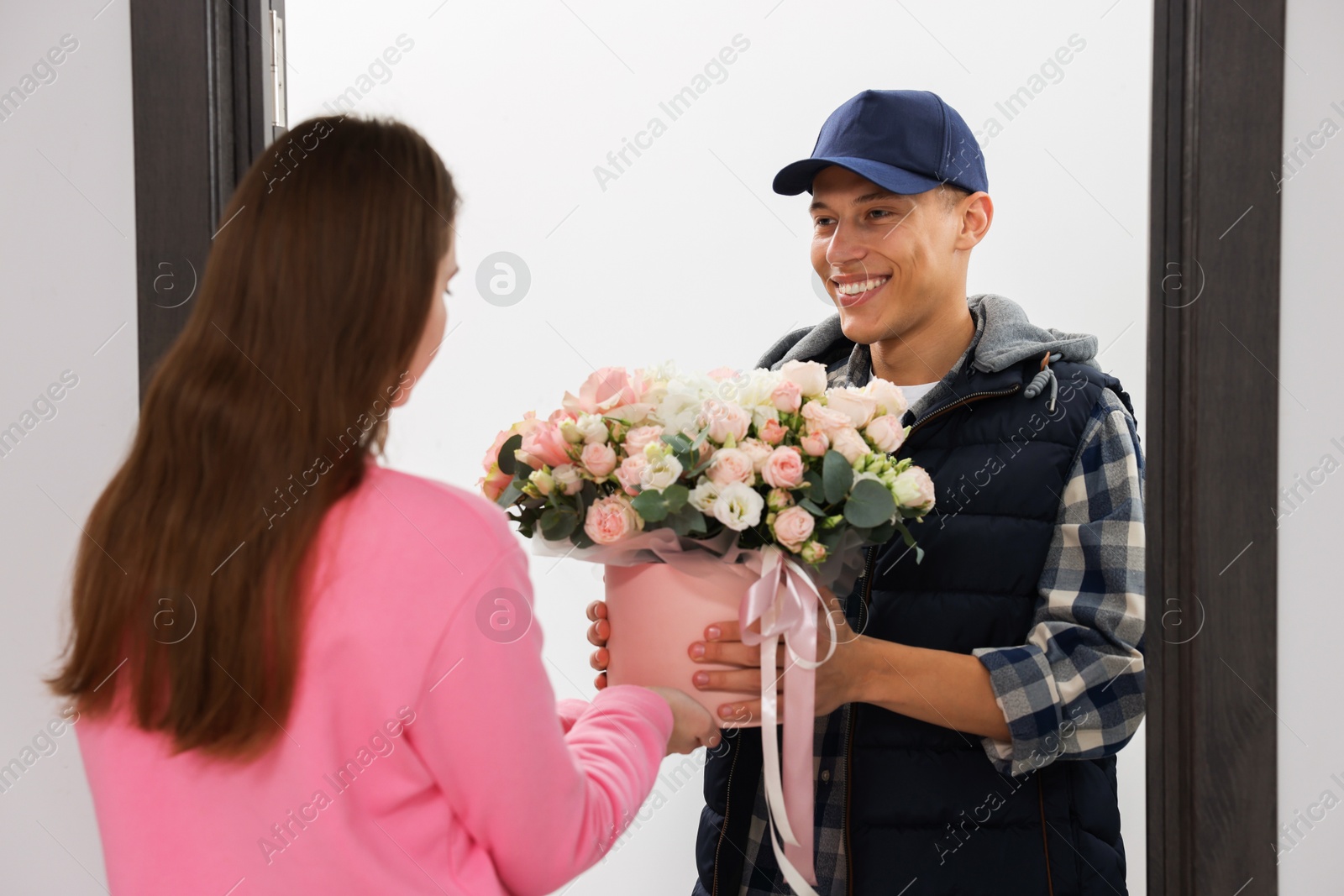 Photo of Happy delivery man giving gift box with beautiful floral composition to woman at door